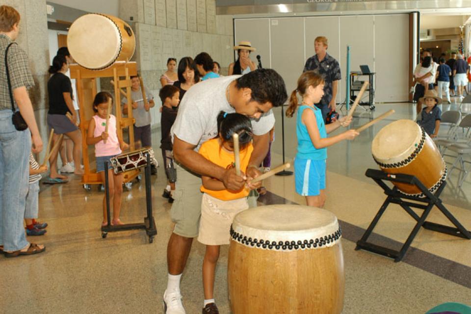 Man holds his daughters hands to guide her in playing taiko